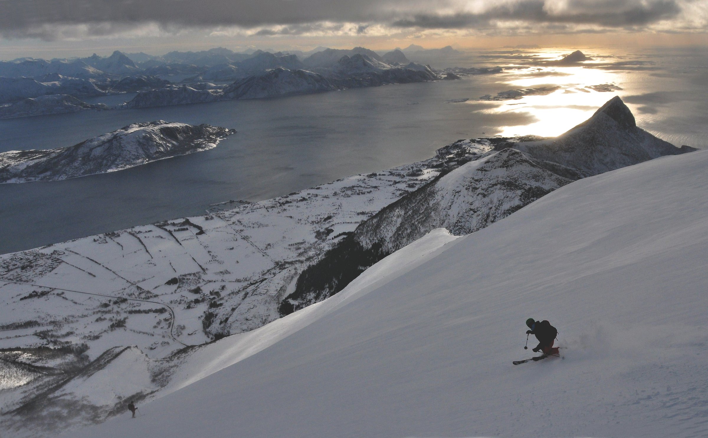 Skikjører på topptur ned sydflanken på Skjeggen ved Reipå, med fjord og kveldslys over havet i bakgrunnen
