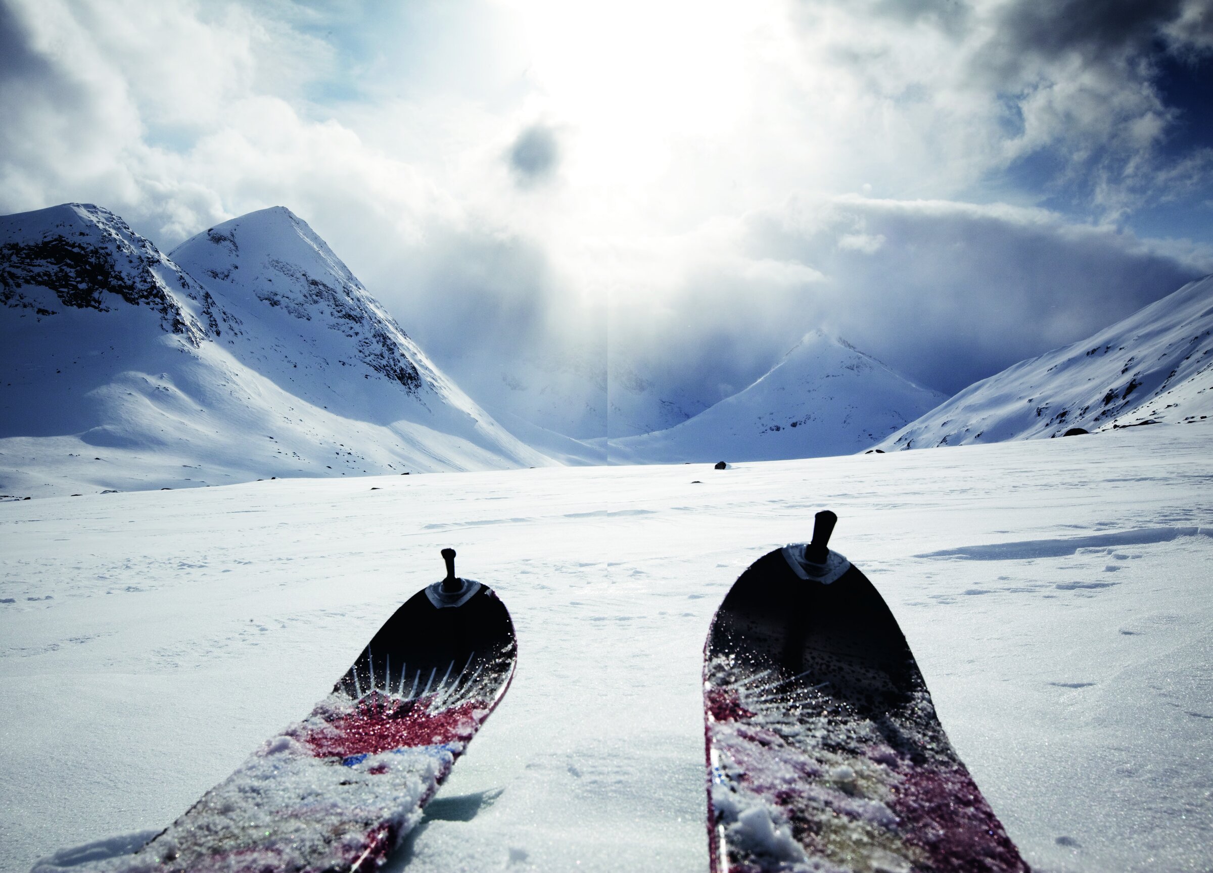 Skituppene til en toppturløper i forgrunnen, med snødekte fjell og dramatisk himmel innover Hunddalen.