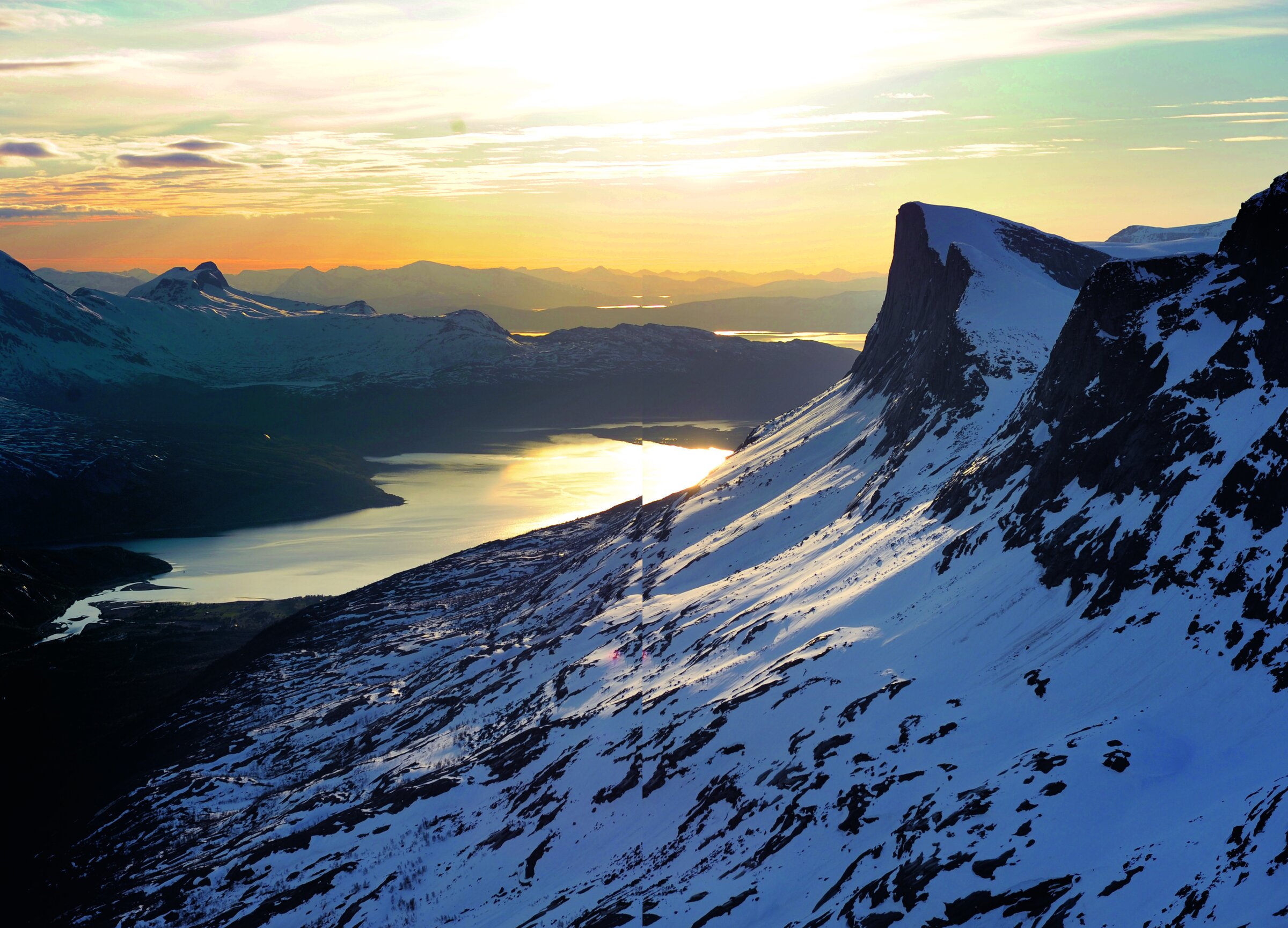 Utsikt fra Skjomdalen i kveldslys, med bratte snødekte granittfjell og fjorden Skjomen som glitrer i solnedgangen.